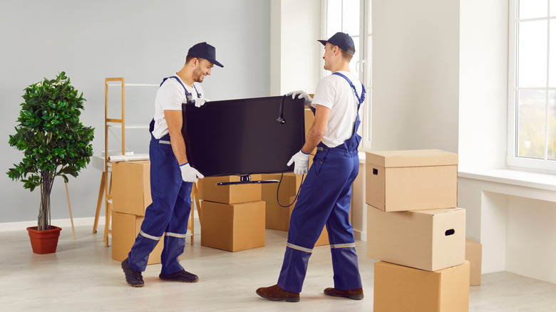 White-gloved deliverymen carrying a TV in a modern living room.