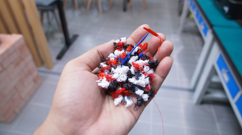 Hand holding a pile of multicolored 3D printer filament waste.