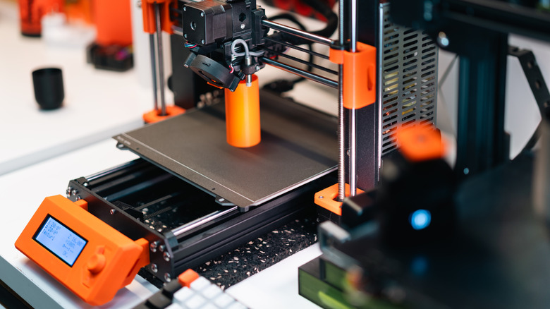 3D printer creating a small orange object on the print bed.
