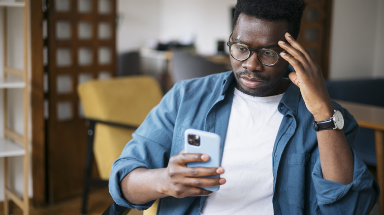 Person sitting in a chair at home holding an iPhone and acting frustrated