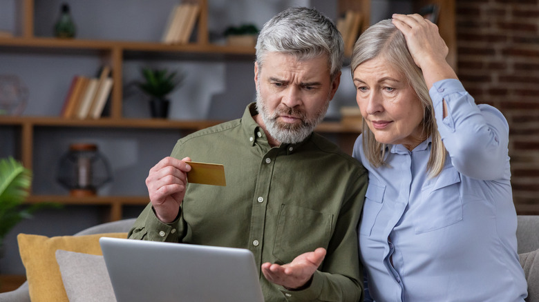 An old couple looking at laptop in a confused state while holding a credit card