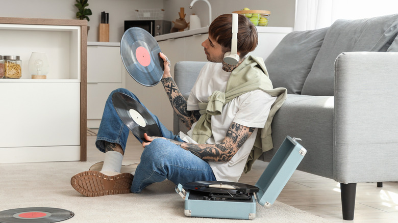 A person listening to a record player with headphones while examining vinyl records