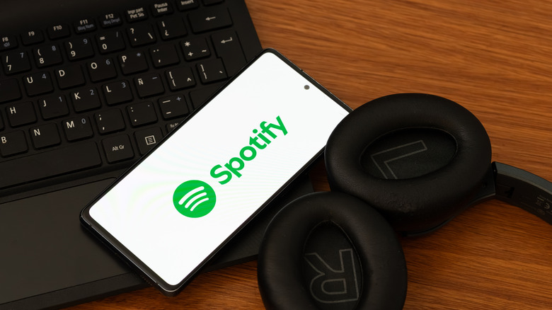 Spotify logo on phone screen laying on laptop next to headphones
