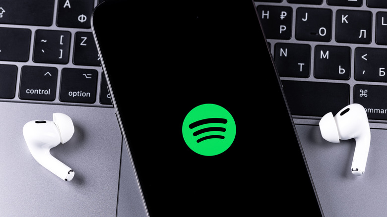 Laptop keyboard with phone sitting on top with Spotify logo on screen