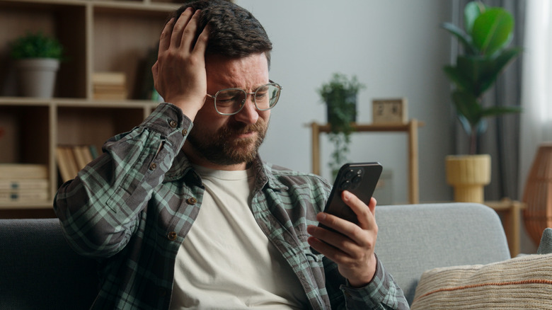 Frustrated man ith hand on head holding and looking at phone