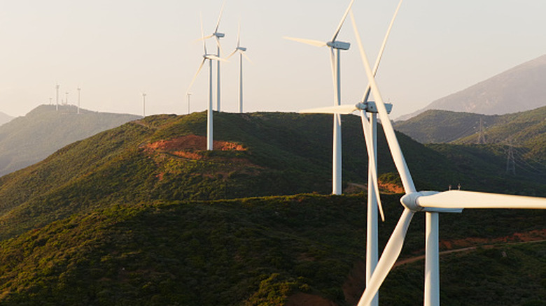 A long row of wind turbines on green hills