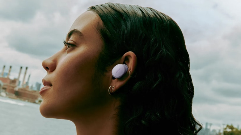 A woman wearing the Bose QuietComfort earbuds with a harbor in the background
