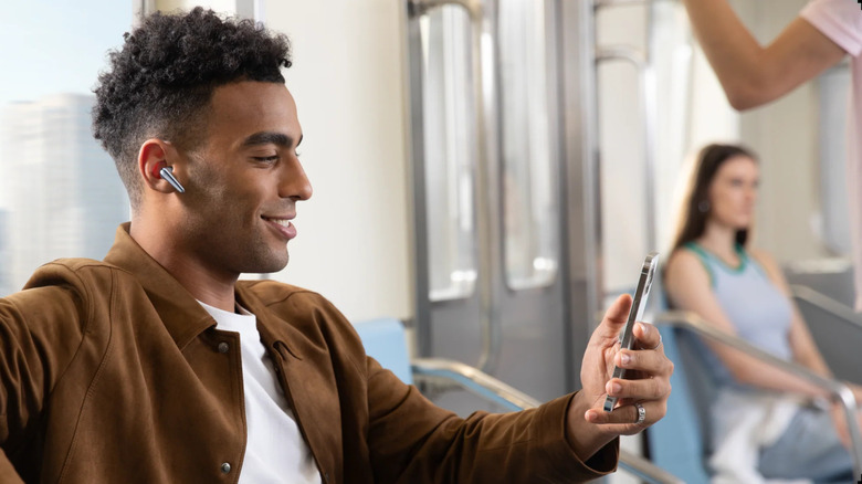 A man wearing the Soundcore Liberty Pro 4 earbuds and looking at his phone on a subway
