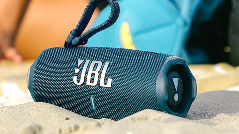 A photo of a black JBL Charge 6 Bluetooth speaker sitting in a pile of sand