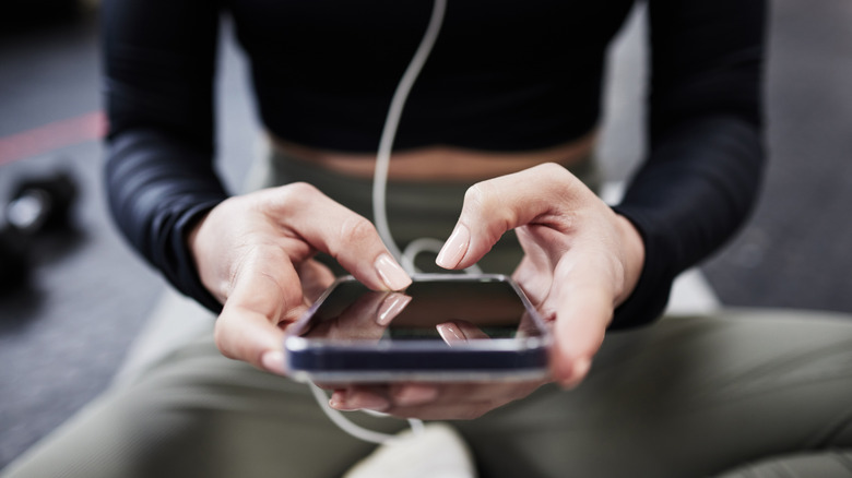 A person sitting down in a gym and holding their smartphone