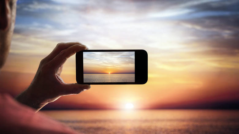 A phone taking a picture of the sun setting over the ocean