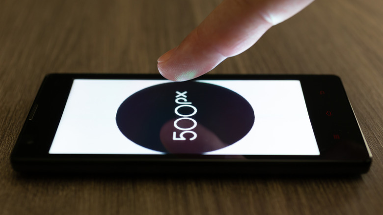 Hand pointing at a phone with the 500px logo displayed