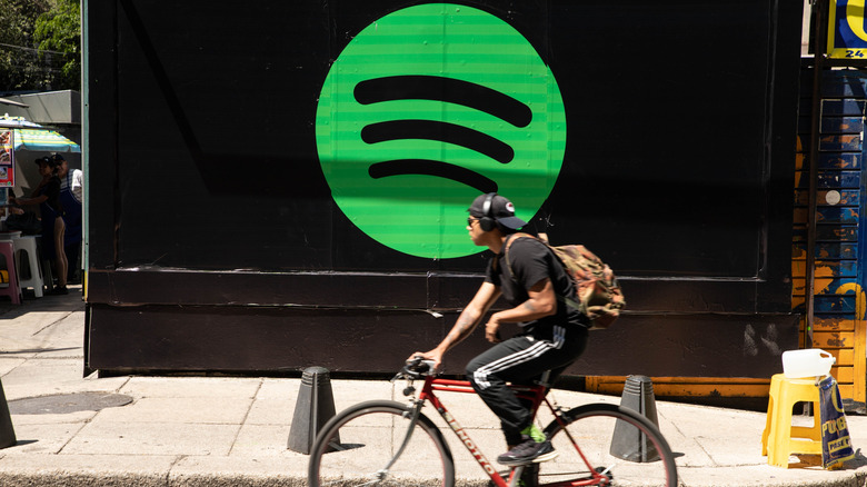 A biker riding past a black wall with the Spotify logo