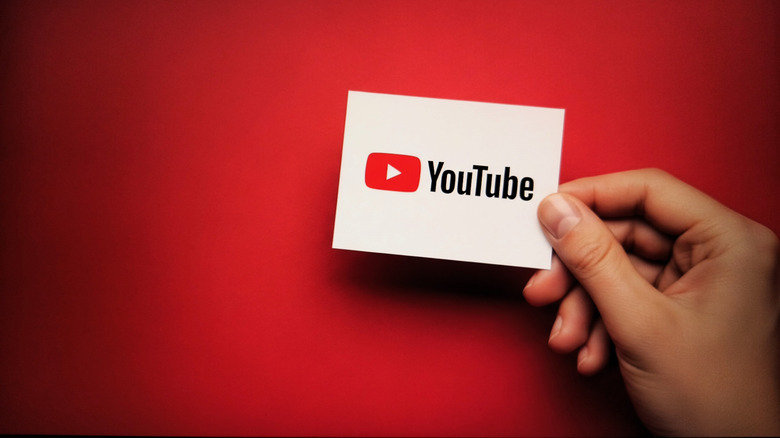 A hand holding a card with the YouTube logo on it against a red and black background