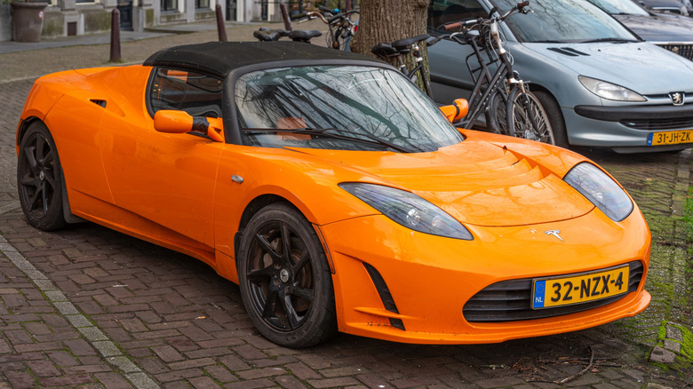 Photo of an orange OG Tesla Roadster parked in a parking lot.