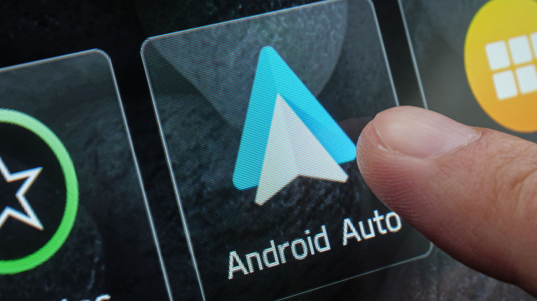 A close-up of a finger pressing the Android Auto logo on a car's infotainment system