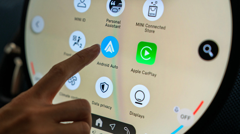 Person touching the Android Auto logo next to an Apple CarPlay app logo on a car infotainment system.