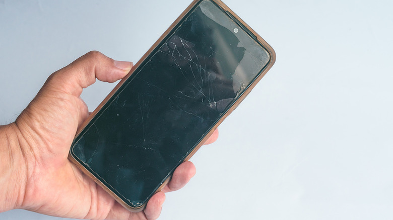 Hand holding phone with cracked screen and case on