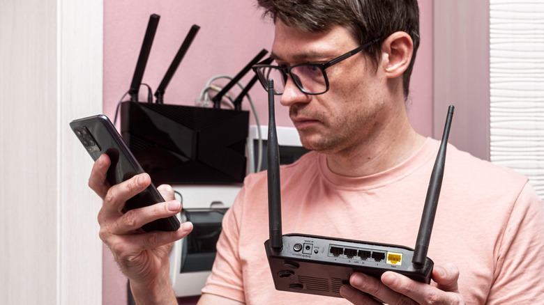A man holding a router and a phone with another router in the background