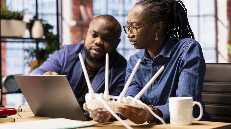 People having a discussion while looking at a computer while one person holds a router