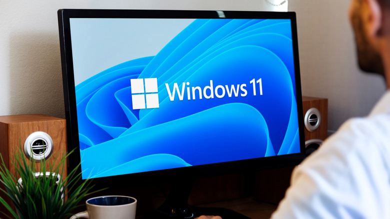 a computer showing the windows 11 logo with a person sitting infront of it
