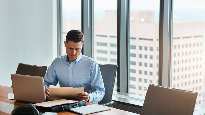 A man looking at files in his office desk by a window.