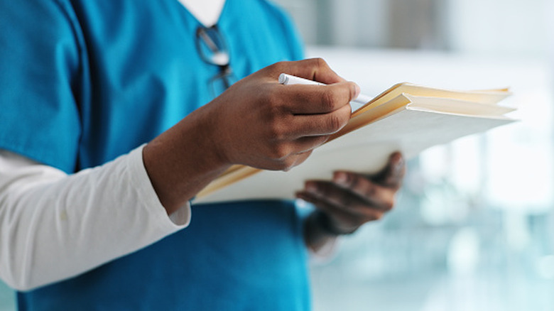 A doctor's torso holding medical files with a pen.