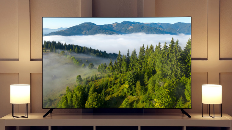 Front view of a thin TV showing a mountain forest, a lamp placed on each side of its screen.