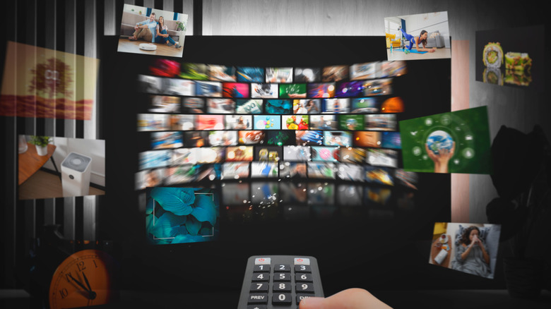 A TV remote being held in front of a TV with the screen displaying a variety of clips, some of them flying out of the screen