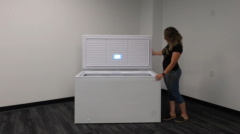 A woman stands next to an open Insignia freezer, where an LED light shines bright.