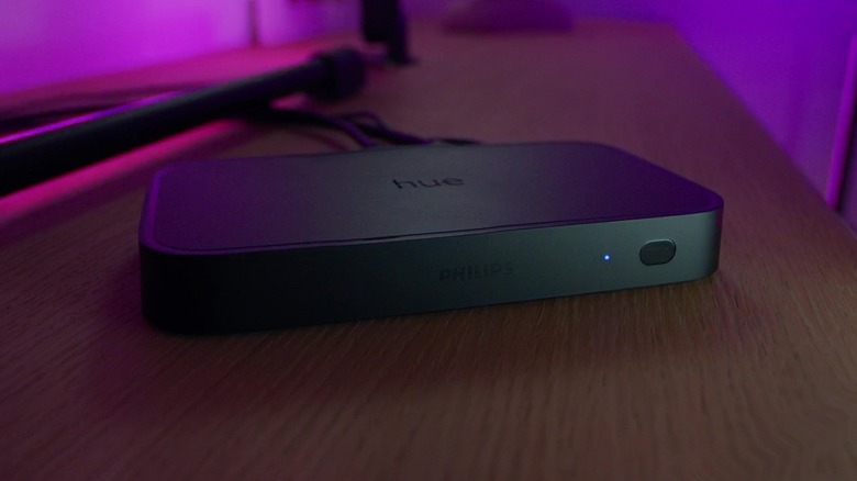 Philips Hue Play HDMI Sync Box 8K on TV stand with lights in the background