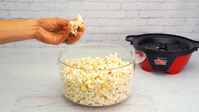 Hand grabbing popcorn from West Bend Stir Crazy Hot Oil Popcorn Popper bowl