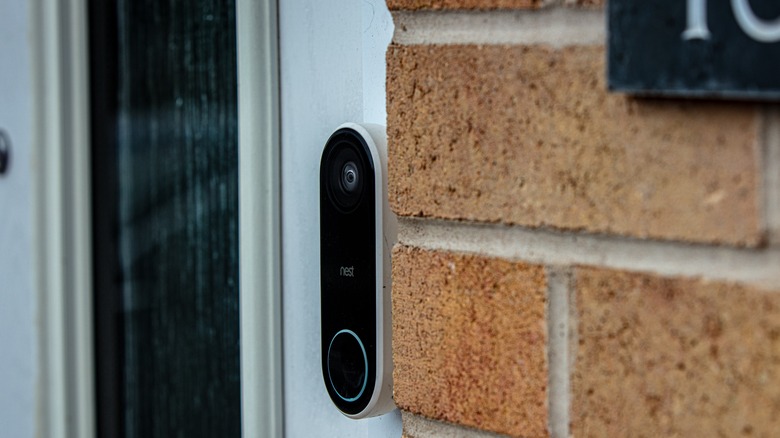 A Google Nest smart video doorbell mounted between a white door and a brick wall