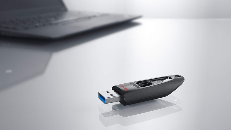 A SanDisk flash drive in the foreground with a faded out computer behind it.