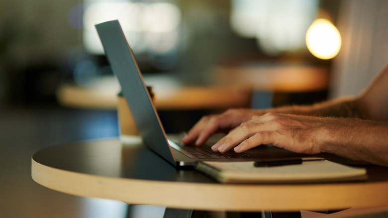 Person typing on a laptop on a small round table
