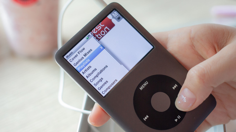 Close up of a hand holding a black iPod Classic with their finger on the click wheel