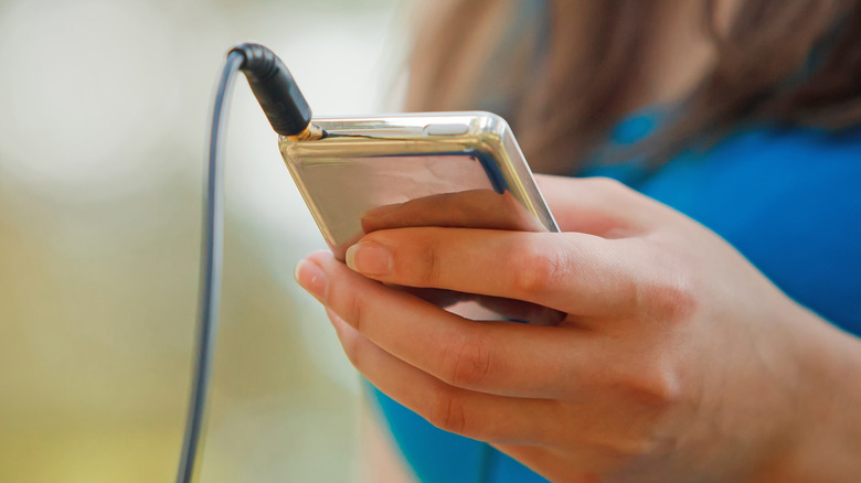 Close up of the back of a classic iPod with a black wire coming out of it in a woman's hand