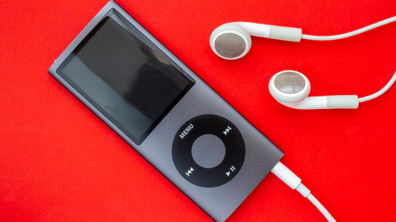 A black iPod Mini with white earbuds plugged into it on a red background