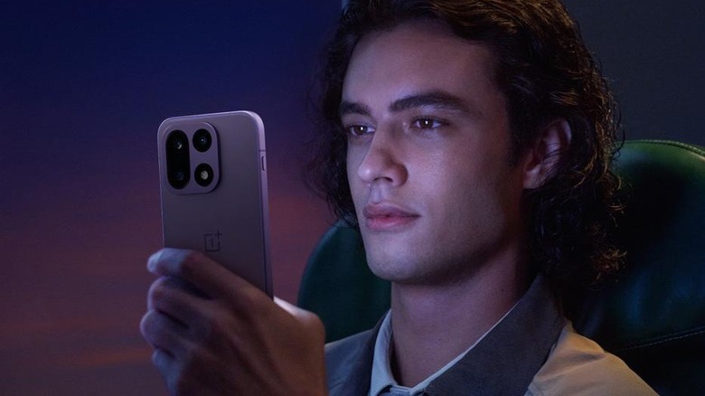 A person looking at the OnePlus 15 smartphone