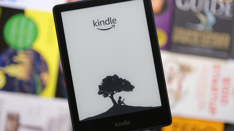 Kindle e-reader showing a black-and-white lock screen in front of blurred book covers.