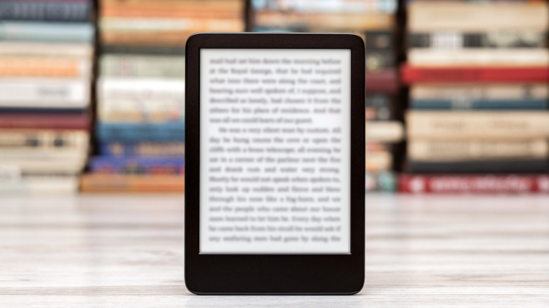 Kindle e-reader displaying a book page with blurred books in the background.