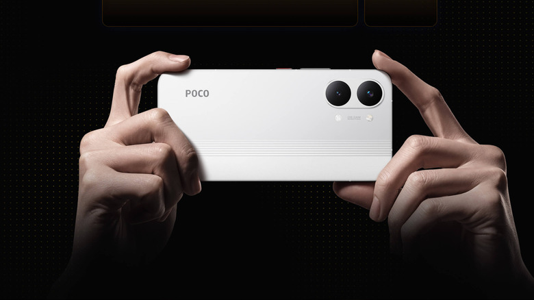 White POCO X8 Pro Max held horizontally with its rear cameras facing forward on a dark background.