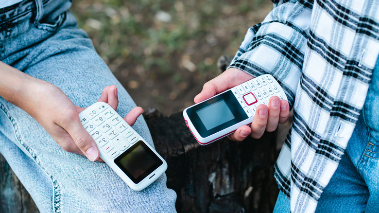 Two dumb phones being held by people