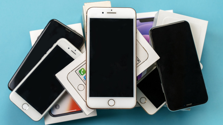 A pile of older iPhones sitting atop a stack of old iPhone boxes, many of the iPhones still have a Home button, indicating their age