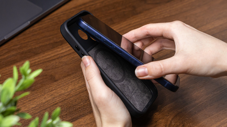 A pair of hands inserting a blue iPhone into a protective case