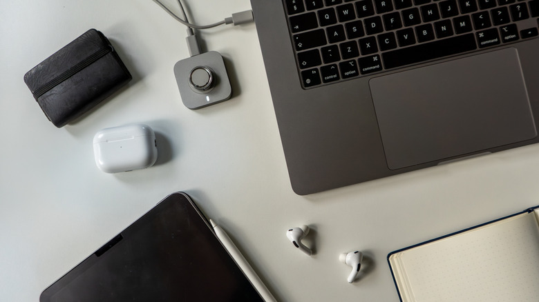 Earbuds on desk with charging dock, laptop, and related components