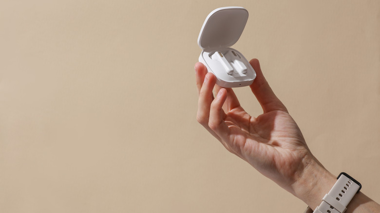 Hands holding earbuds in charging case against tan background
