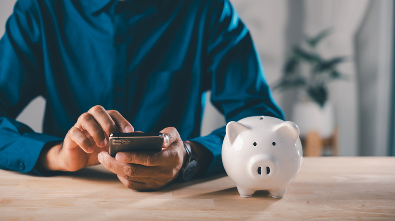 A person sitting by a piggy bank while interacting with their phone