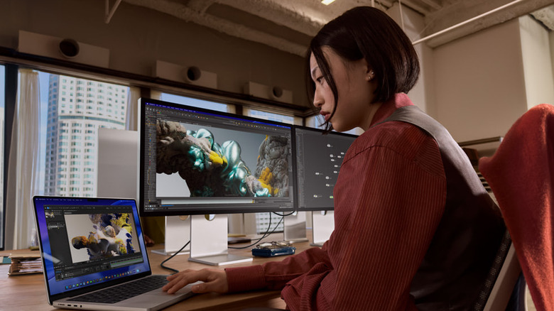 woman sits at work station using mac and two apple studio display monitors