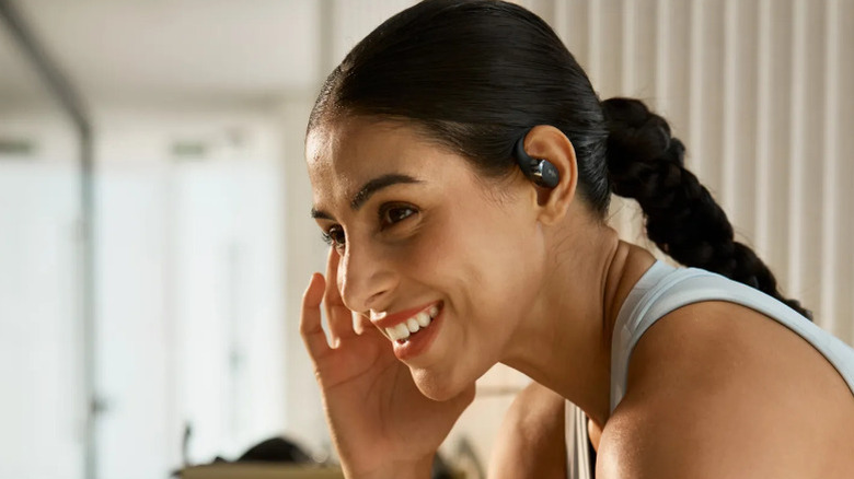 Women stands in front of clear blue sky listening to SHOKZ OpenFit 2 headphones